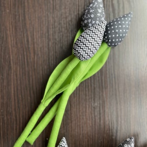 May include: A bouquet of three black and white fabric tulips with green stems. The tulips have different patterns: one with polka dots, one with zigzags, and one with a floral pattern.
