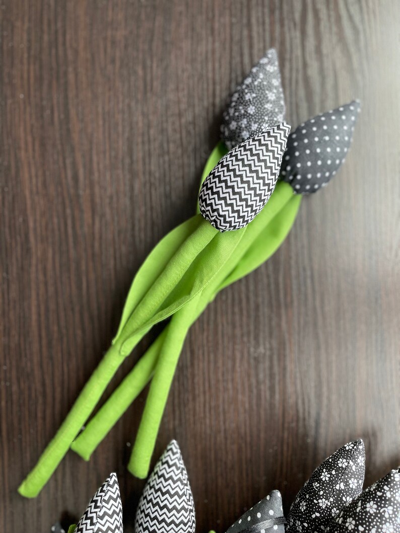 May include: A bouquet of three black and white fabric tulips with green stems. The tulips have different patterns: one with polka dots, one with zigzags, and one with a floral pattern.