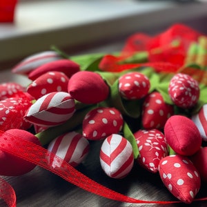 Puede incluir: Un ramo de tulipanes de tela roja y blanca con tallos verdes. Los tulipanes est&aacute;n dispuestos en forma de abanico y est&aacute;n atados con una cinta roja.