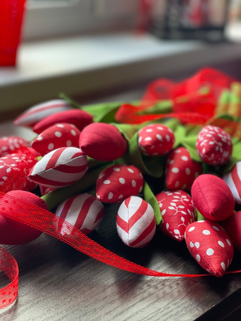Puede incluir: Un ramo de tulipanes de tela roja y blanca con tallos verdes. Los tulipanes est&aacute;n dispuestos en forma de abanico y est&aacute;n atados con una cinta roja.