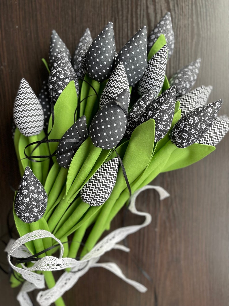 May include: A bouquet of black and white fabric tulips with green stems tied together with a white lace ribbon.