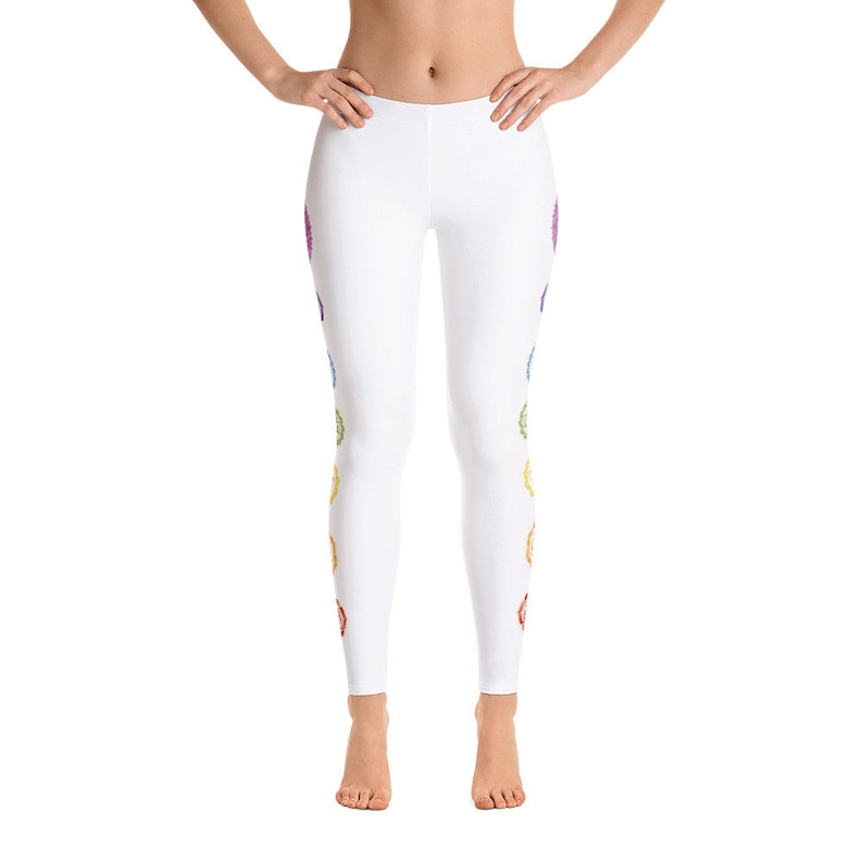 May include: White leggings with a colorful chakra design. The leggings feature a series of seven vibrant, rainbow-colored symbols running down the sides. The design is symmetrical, with the same pattern on both legs. The leggings are made of a soft, stretchy material.