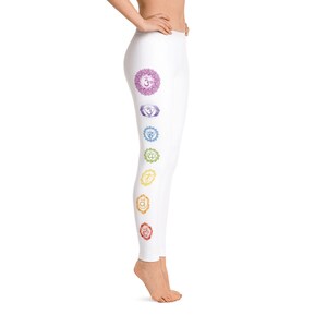 May include: White leggings featuring a series of colorful chakra symbols down the side. The symbols are in shades of purple, blue, green, yellow, orange, and red. The leggings are made of a soft, stretchy material.