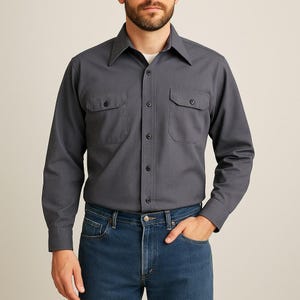 May include: A charcoal gray long-sleeve shirt with two chest pockets and a button-down front. The shirt is paired with blue denim jeans. The shirt has a classic collar and buttoned cuffs. The model is wearing a white undershirt.