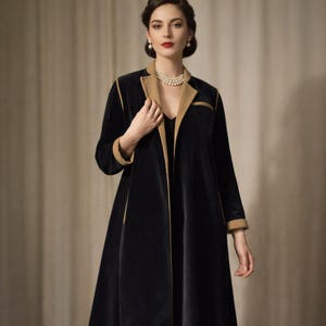 May include: A black velvet coat with tan trim and lapels. The long coat has a classic design with a tailored fit. The sleeves have tan cuffs. The woman in the image is wearing a pearl necklace and earrings.