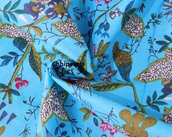 May include: Blue fabric with a white and green floral print. The fabric has a textured surface and a slightly wrinkled appearance. The fabric is folded in half and the print is visible on both sides.