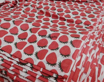 May include: A stack of white fabric with a red strawberry print. The fabric is folded neatly and the strawberries are evenly spaced.