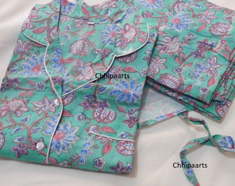 Op de afbeelding: Een pyjamaset met een groene en roze bloemenprint en een witte bies. Het bovenstuk heeft een knoopsluiting en een kraag. De broek heeft een elastische tailleband.