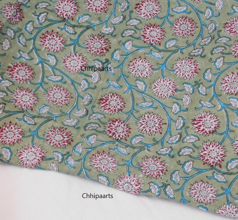 May include: Green fabric with a white and red floral pattern. The fabric has a blue outline around the flowers and leaves. The text "Chhipaarts" is printed on the fabric.