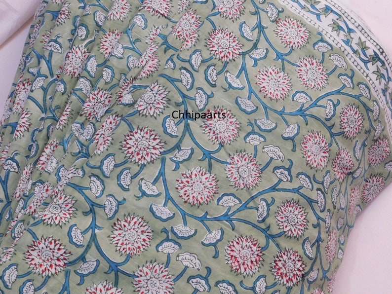 May include: Green fabric with a white and blue floral pattern. The fabric has a white border with a blue and white star pattern.