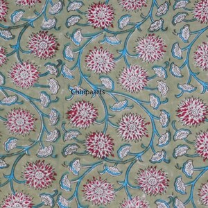 May include: A green fabric with a repeating pattern of white and pink flowers with blue stems and leaves. The fabric has the text "Chhipaarts" printed on it.