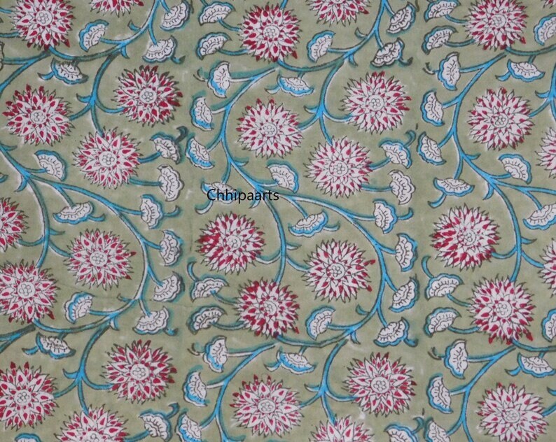 May include: A green fabric with a repeating pattern of white and pink flowers with blue stems and leaves. The fabric has the text "Chhipaarts" printed on it.