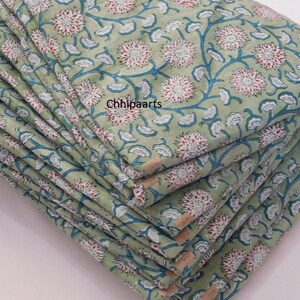 May include: A stack of green fabric with a white and blue floral print. The fabric is folded in half and the print is visible on both sides. The fabric is a light green color with a white and blue floral print. The fabric is folded in half and the print is visible on both sides.