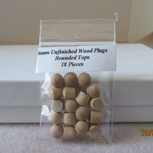 May include: A bag containing 18 unfinished wood plugs with rounded tops. The bag is labelled "6mm Unfinished Wood Plugs Rounded Tops 18 Pieces".