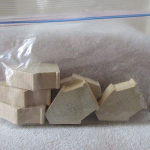 May include: A plastic bag containing several wooden hexagonal pieces. The pieces are stacked on top of each other and have a light brown colour.
