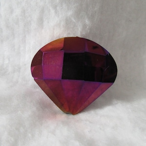 May include: A large, faceted, iridescent gemstone in the shape of a diamond. The gemstone is a deep red colour with hints of purple and blue.