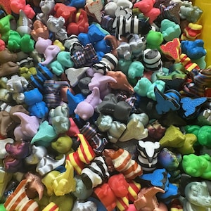 May include: A close-up shot of a large assortment of colorful, small, plastic figurines. The figurines are in various shapes, including animals and abstract forms, and are in a variety of colors, including red, blue, green, and black and white.