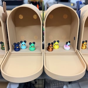 May include: Four beige mailboxes, each with a different assortment of colorful mouse figurines inside. The mice are various colors, including red, blue, yellow, and pink. The mailboxes have open trays and arched tops.