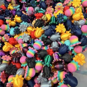 May include: A vibrant assortment of colorful, 3D-printed shapes, including flowers, octopuses, and abstract designs. The collection features a variety of colors, including pink, yellow, blue, and black. These decorative items are ideal for crafting or as unique embellishments.