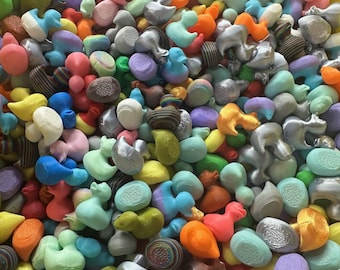 May include: A vibrant assortment of colorful, abstract duck-shaped figurines. The collection features a variety of hues, including pink, blue, green, orange, and silver. The figurines appear to be made of a smooth material.