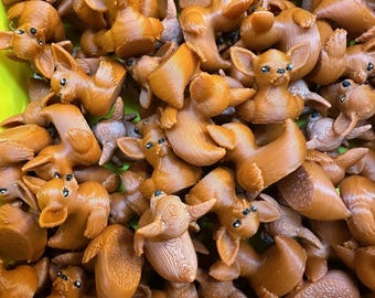 May include: A collection of small, brown, 3D-printed figurines of a cartoon dog with large ears and small eyes. The figurines are scattered, with some facing different directions. The overall color is a warm brown.
