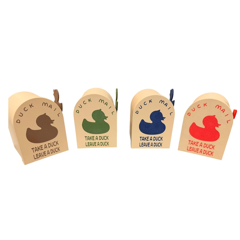 May include: Four small, beige cardboard mailboxes with a duck theme. Each box features a different colored duck graphic (brown, green, blue, and red) and the text "DUCK MAIL" and "TAKE A DUCK LEAVE A DUCK". The mailboxes have small flags.