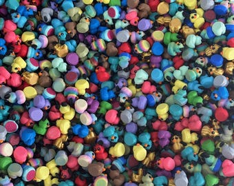 May include: A vibrant assortment of miniature duck figurines in various colors, including yellow, blue, red, and purple. The ducks have black eyes and some have additional decorative elements. The image is a close-up, showing the figurines densely packed together.