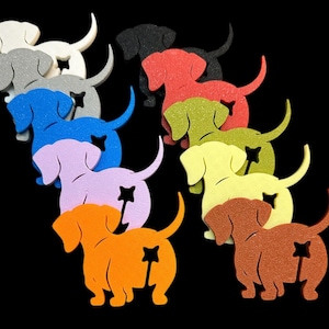 May include: A collection of colorful dachshund dog cutouts in various colors, including white, gray, blue, purple, orange, brown, yellow, green, red, and black. Each dog has a star-shaped cutout on its rear. The background is black.