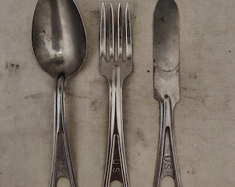 May include: A set of three vintage silver-colored utensils: a spoon, a fork, and a knife. Each piece has a handle with a teardrop-shaped opening and the letters "U.S." stamped on it. The spoon has a large, oval bowl.
