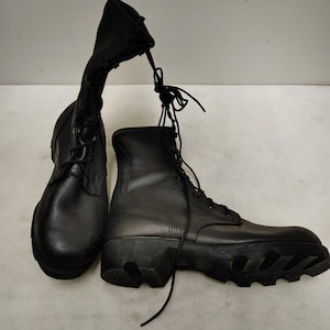 Puede incluir: Un par de botas de combate negras con caña alta y suelas de goma gruesas y con tacos. Las botas cuentan con cordones negros atados en la parte superior, una puntera redondeada y un acabado mate y liso en la superficie exterior de cuero.