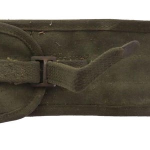 May include: An olive green canvas utility pouch featuring a rectangular shape with rounded corners. The pouch includes a flap closure secured by a matching fabric strap and a metal buckle, along with a fabric loop attachment on the left side.