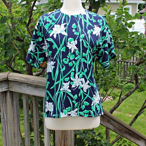 May include: A navy blue short-sleeved blouse with a white and green floral print. The flowers are stylized and have a delicate, almost abstract look.