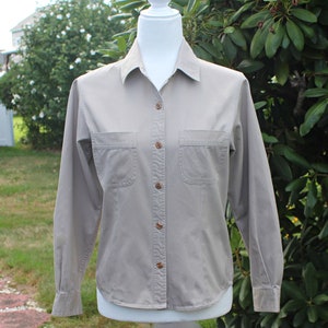 May include: A long-sleeved, light gray button-down shirt with two chest pockets. The shirt has a collared neckline and a button closure.