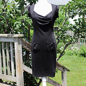 May include: A black sleeveless dress with a scoop neck and a fitted silhouette. The dress has two pockets on the front and a small button detail on each pocket.