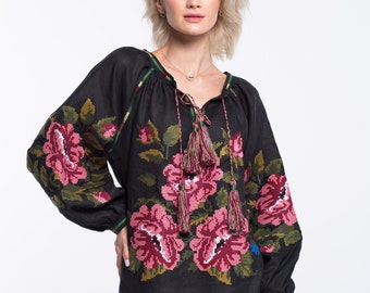 May include: Black linen blouse with embroidered pink flowers and green leaves. The blouse has a V-neck and long sleeves with tassels at the neckline.