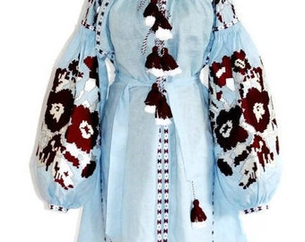 May include: A light blue linen dress with embroidered floral patterns in white and burgundy. The dress has long sleeves with a gathered cuff and a tie belt. The dress is decorated with white and burgundy tassels.