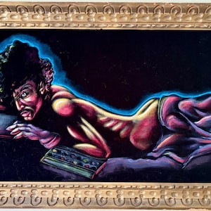 May include: A framed painting featuring a reclining figure with a dark complexion, rendered in vibrant reds, purples, and blues. The artwork has a dramatic, stylized aesthetic, with a gold-colored ornate frame. The figure is positioned on a dark background.