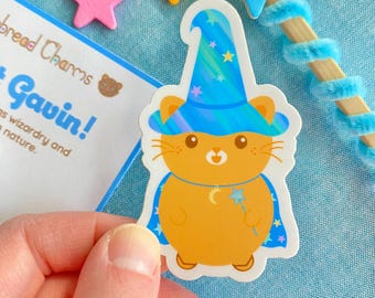 Könnte beinhalten: Ein Aufkleber mit einer Cartoon-Katze in Orange, die einen blauen Zaubererhut mit Sternen und einem Halbmond trägt. Die Katze hält einen Zauberstab mit einem Stern am Ende. Der Aufkleber befindet sich auf einem blauen Hintergrund.