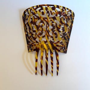 Puede incluir: Un peine para el cabello de carey marrón y amarillo con un diseño decorativo calado. El peine tiene cinco dientes.