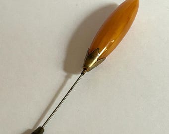 May include: A vintage amber glass hat pin with a gold-toned metal base and a pointed tip.