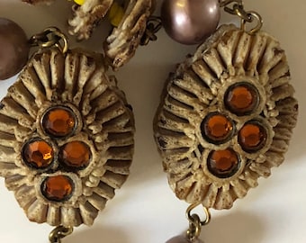 Puede incluir: Primer plano de un collar con cuentas marrones texturizadas, algunas con diamantes de imitación naranjas, y cuentas marrón claro. El collar también tiene algunas cuentas rosa claro.