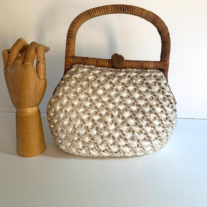 May include: A vintage handbag with a woven, off-white body and a curved, brown rattan handle. The bag features a wooden clasp and a textured, open weave design. The bag is a small, handheld size.