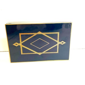 Può includere: Una scatola rettangolare blu scuro con un design geometrico dorato. Il design presenta una forma a diamante all'interno di una forma a diamante più grande.