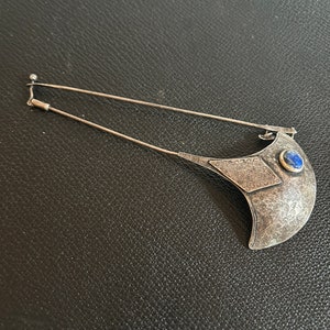 May include: A silver brooch with a blue stone and intricate filigree design.