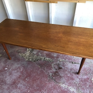 May include: A long, rectangular, wooden coffee table with a light brown finish and tapered legs.