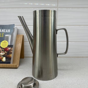 May include: A stainless steel oil and vinegar dispenser with a spout and a lid. The dispenser is on a white countertop.