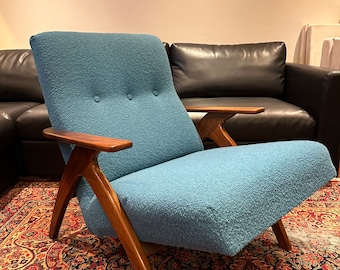 May include: A blue armchair with a tufted back and wooden arms. The chair is sitting on a patterned rug.