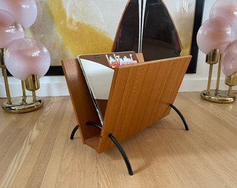 May include: A wooden magazine rack with black metal legs. The rack is open and has a few records inside.