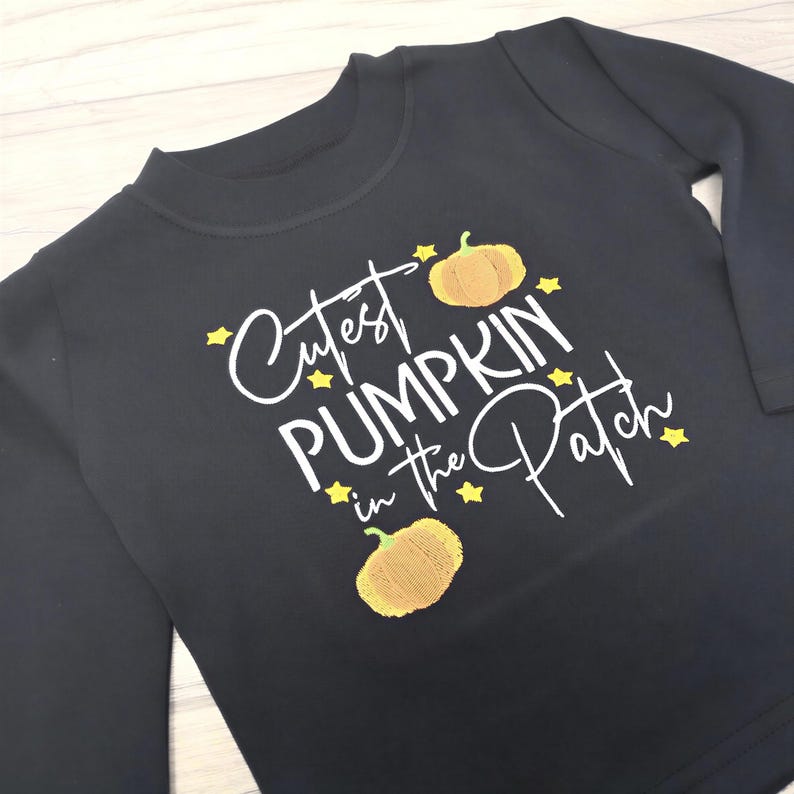 Long sleeve black t-shirt embroidered with black text reading Cutest Pumpkin in the Patch and  orange pumpkins and little yellow stars.
