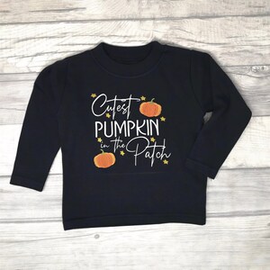 Long sleeve black t-shirt embroidered with black text reading Cutest Pumpkin in the Patch and  orange pumpkins and little yellow stars.